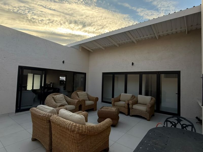 A spacious covered patio featuring tiled flooring, built-in braai, and large sliding doors providing seamless access to the interior living areas.