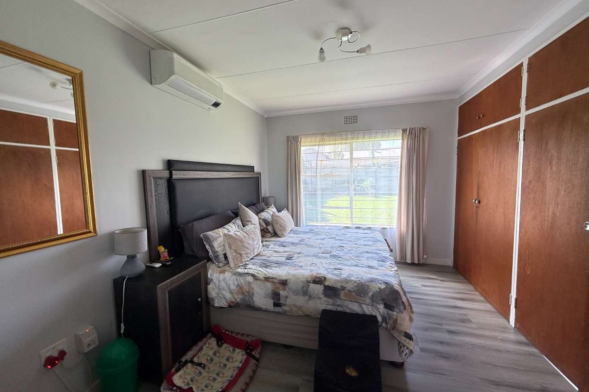 A well-lit bedroom featuring wood-look laminate flooring, built-in wooden wardrobes, and a wall-mounted air conditioning unit.