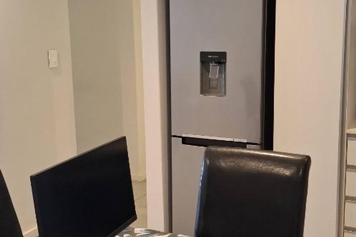 A modern kitchen area featuring sleek white cabinetry, integrated appliance housing, and recessed ceiling lighting in an open-plan apartment layout.