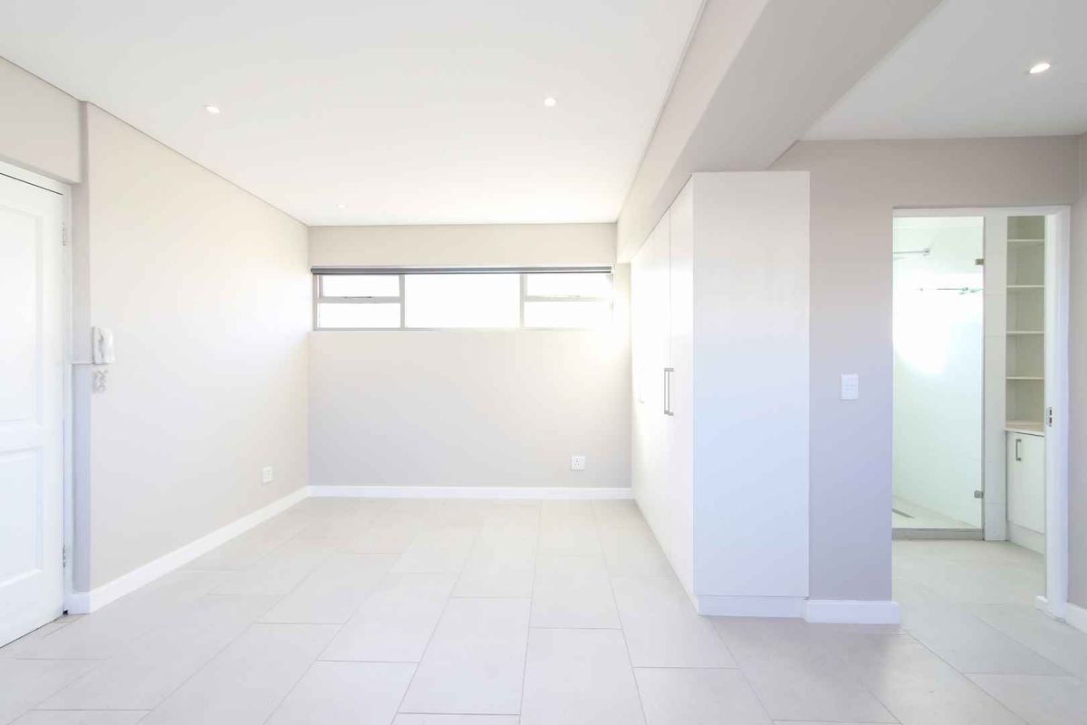 A bright, modern bedroom featuring neutral tiled flooring, built-in cabinetry, and an en-suite bathroom with a walk-in shower.