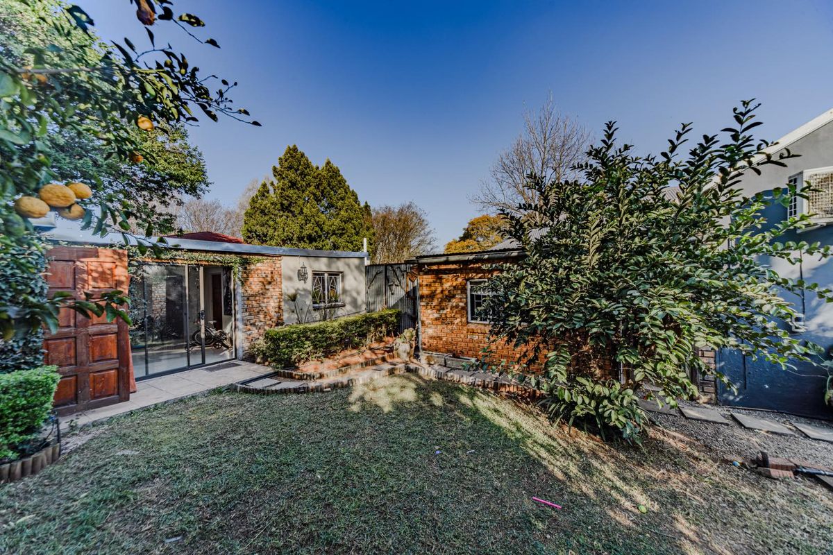 A rear exterior view of the property featuring exposed brick walls, a paved patio area, and a landscaped garden space.