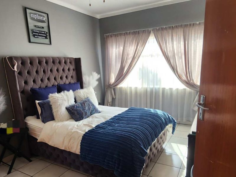 A well-maintained bedroom featuring neutral grey walls, tiled flooring, and natural light through window curtains.