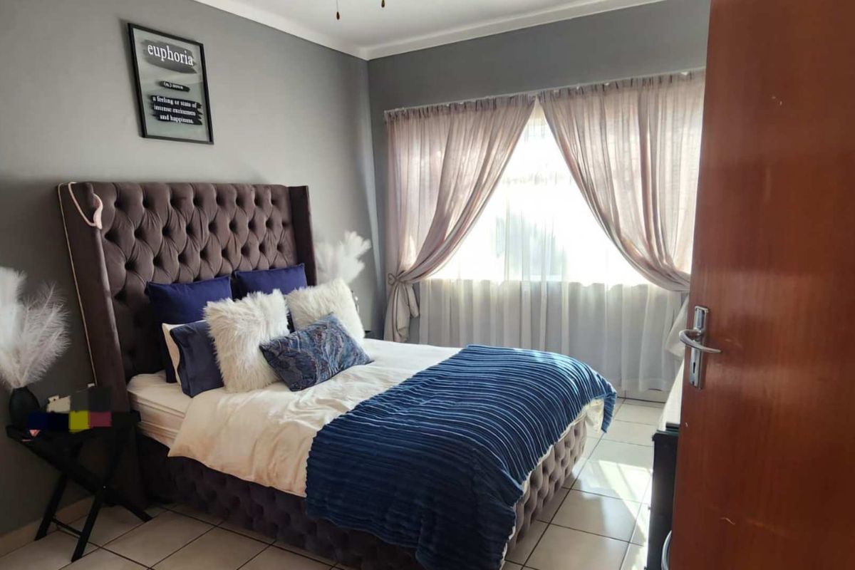 A well-maintained bedroom featuring neutral grey walls, tiled flooring, and natural light through window curtains.
