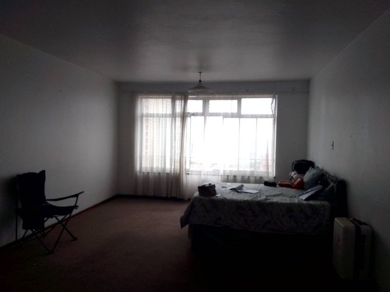 A spacious bedroom featuring a large window with natural light, carpeted flooring, and a neutral wall finish.