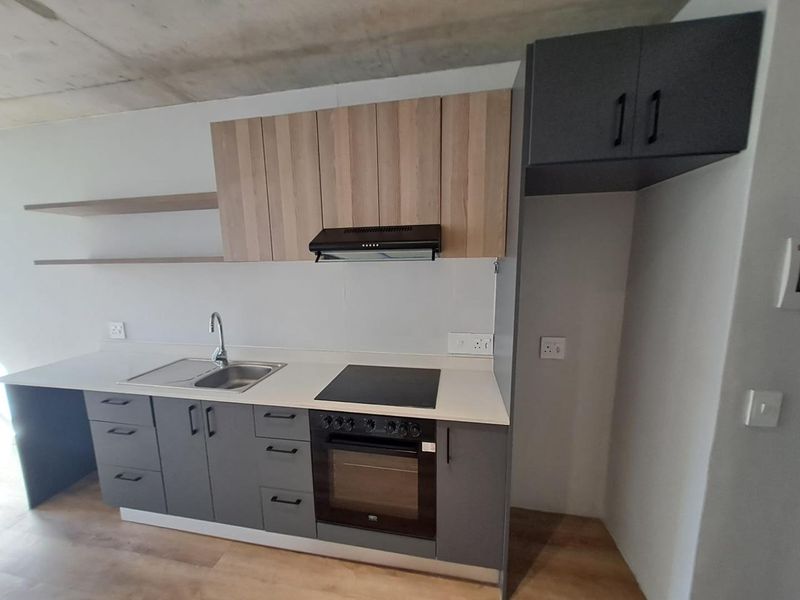 Modern kitchen featuring two-tone cabinetry, built-in oven, electric hob, extractor fan, stainless steel sink, and floating shelves with an exposed concrete ceiling.