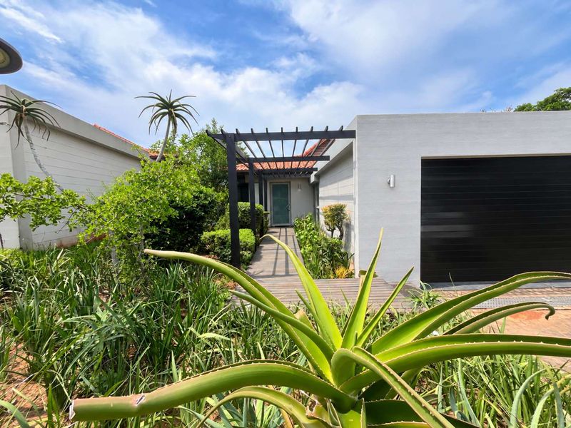 Front entrance of the townhouse featuring a timber walkway, a modern pergola, and a well-maintained landscaped garden leading to the front door.