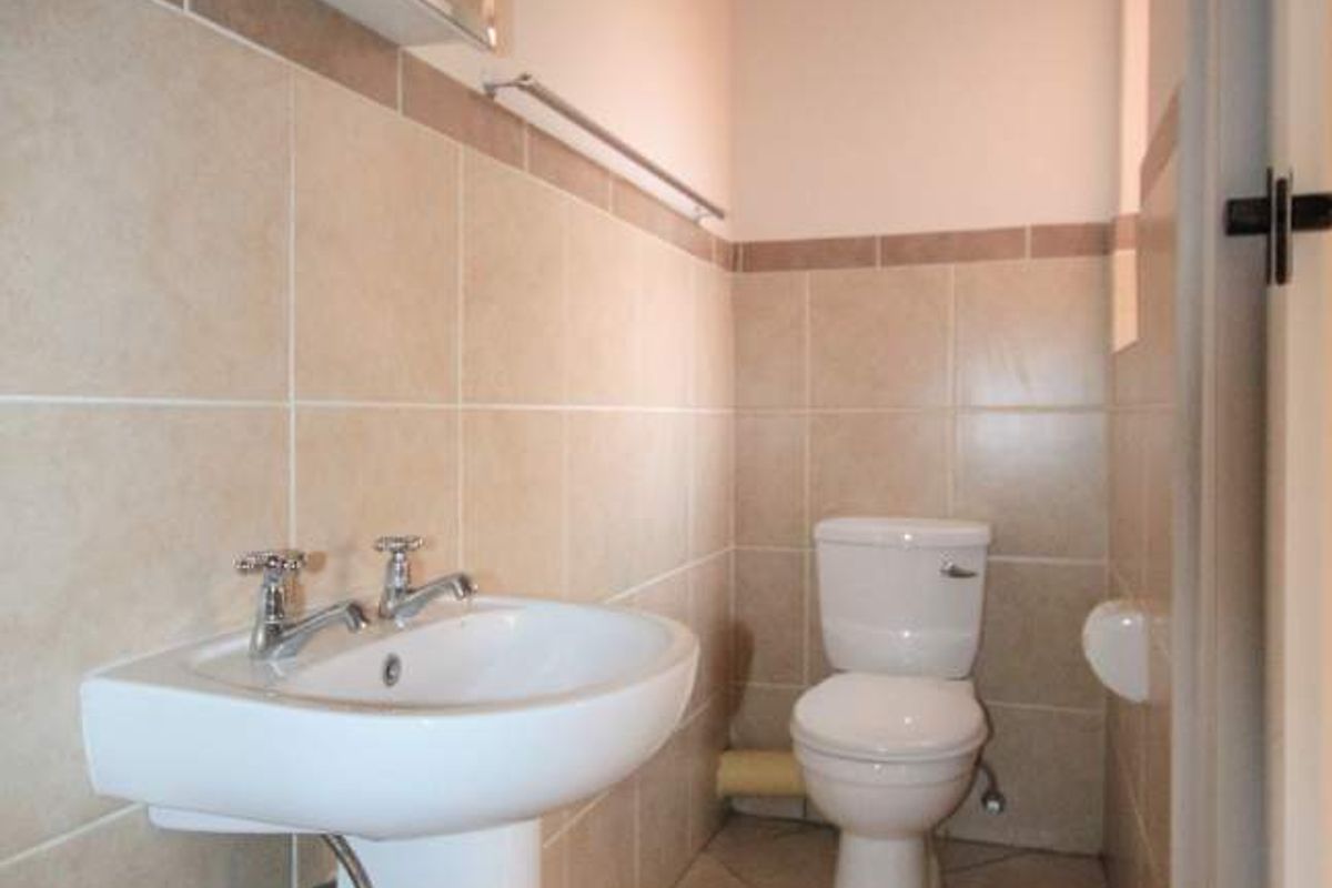 A functional bathroom featuring a pedestal basin, toilet, and wall-mounted medicine cabinet with neutral ceramic tiling throughout.