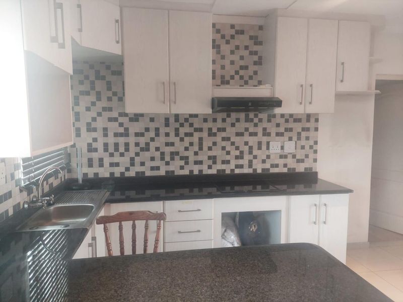 A functional kitchen featuring granite countertops, mosaic tile backsplash, built-in cabinetry, and an integrated extractor fan, with space prepared for an oven installation.