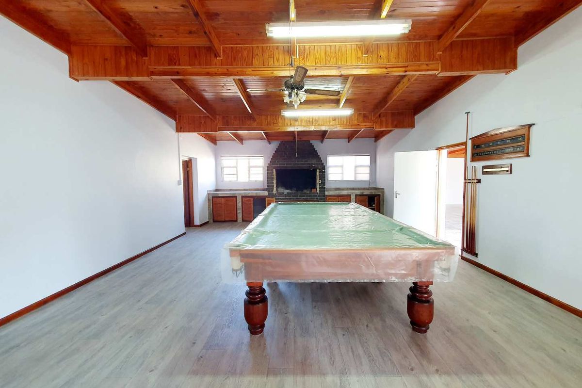 Spacious entertainment room featuring a prominent brick fireplace, exposed timber beam ceiling, and modern light-toned laminate flooring.