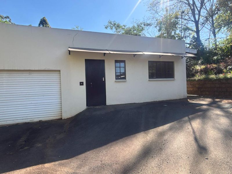 Exterior view of a cottage garage featuring a roller shutter door, an awning, and an adjacent asphalt driveway.
