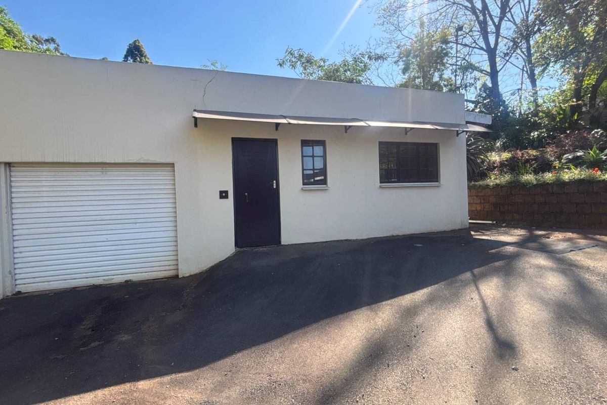 Exterior view of a cottage garage featuring a roller shutter door, an awning, and an adjacent asphalt driveway.
