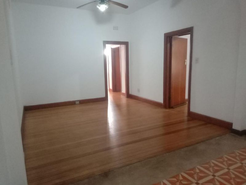 An empty living room featuring polished hardwood flooring, timber door frames, and a ceiling fan, offering a blank canvas for interior design.