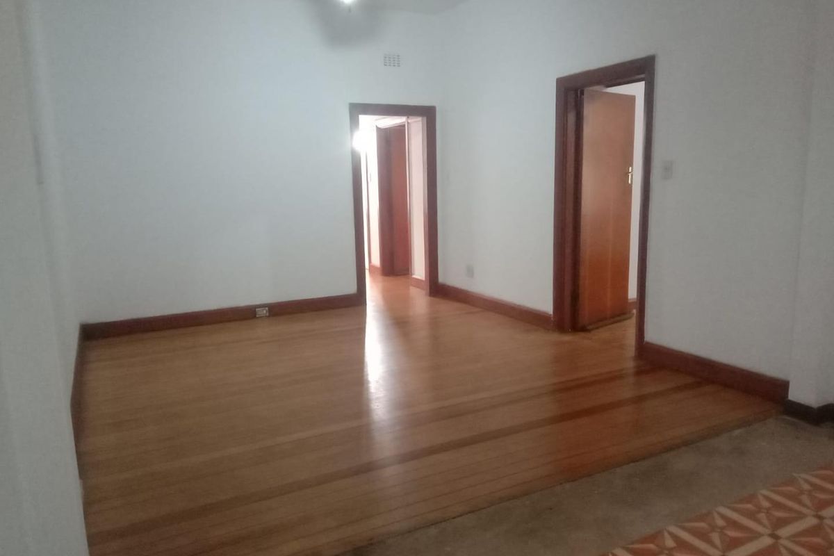 An empty living room featuring polished hardwood flooring, timber door frames, and a ceiling fan, offering a blank canvas for interior design.