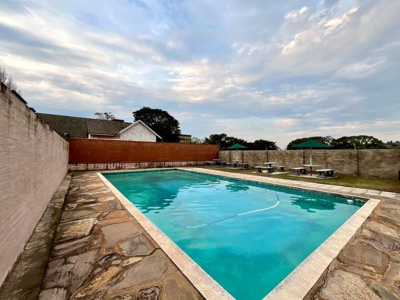 Communal swimming pool area featuring stone paving, perimeter brick and stone walls, and a dedicated outdoor seating space.