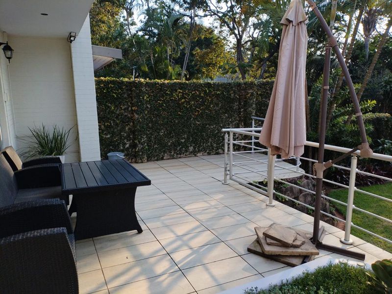 A spacious outdoor patio featuring tiled flooring, a metal safety balustrade, and a lush green climbing plant wall, perfect for outdoor relaxation.
