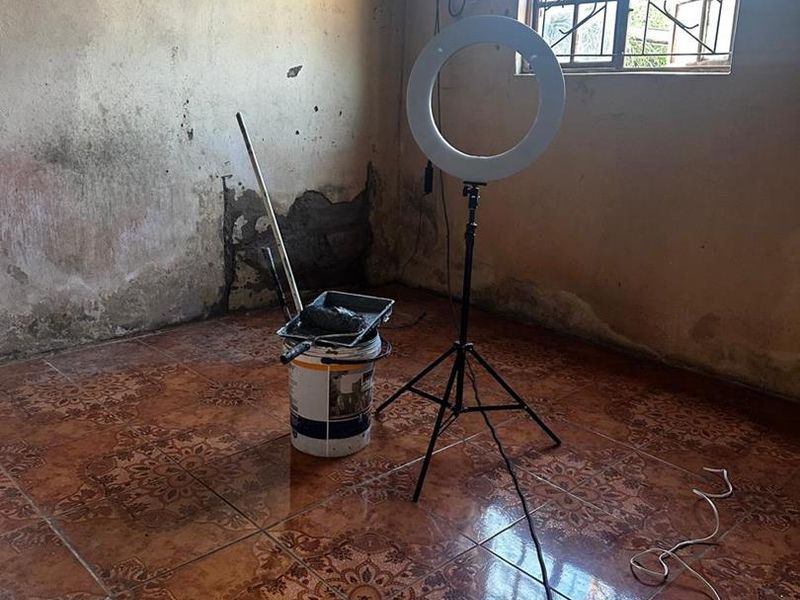 An empty bedroom featuring tiled flooring and security bars on the window, currently requiring significant wall repairs and cosmetic renovation.
