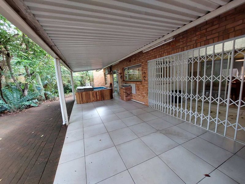 Spacious covered patio featuring tiled flooring, a built-in brick braai, and security gates, providing a functional outdoor entertainment area.