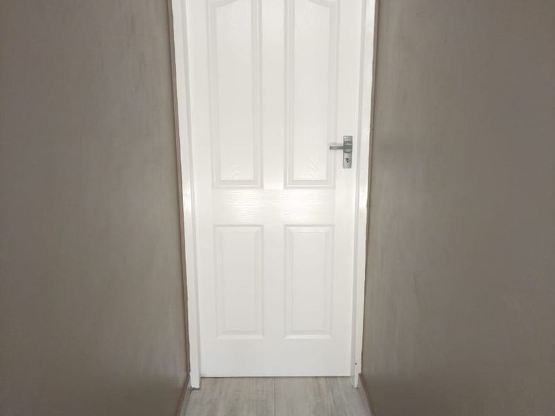 A clean and simple hallway featuring neutral wall tones and light-colored tiled flooring leading to an internal door.