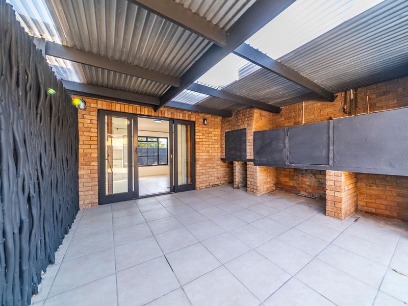 Covered patio area featuring a built-in braai, tiled flooring, and sliding glass doors providing access to the interior living space.