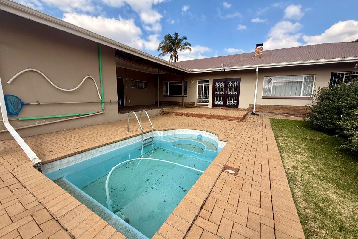 Rear exterior view featuring a swimming pool, brick paved patio area, and covered outdoor space attached to the main house structure.