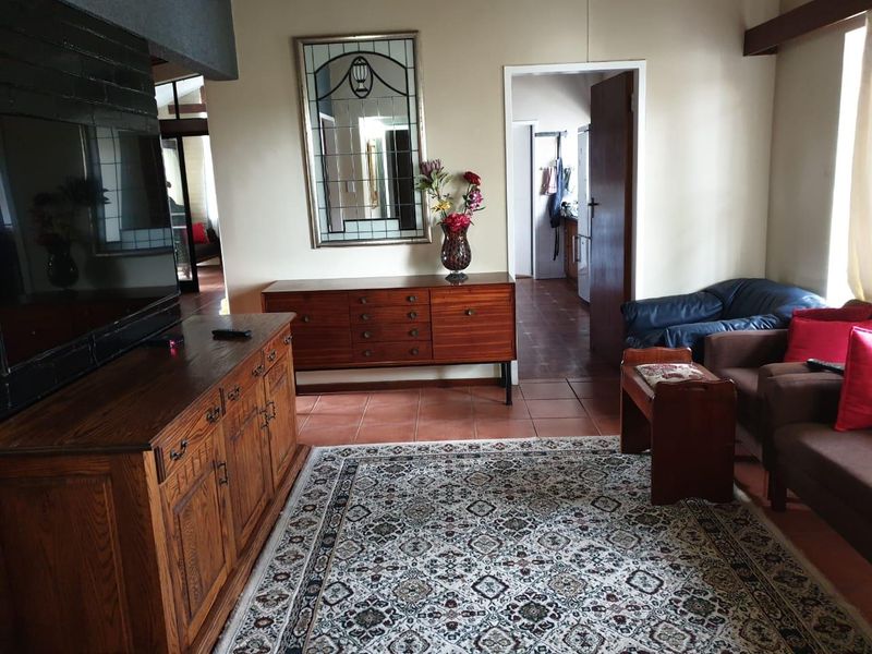 A living room featuring terracotta floor tiles and a brick fireplace surround, with an open doorway leading to an adjacent kitchen area.
