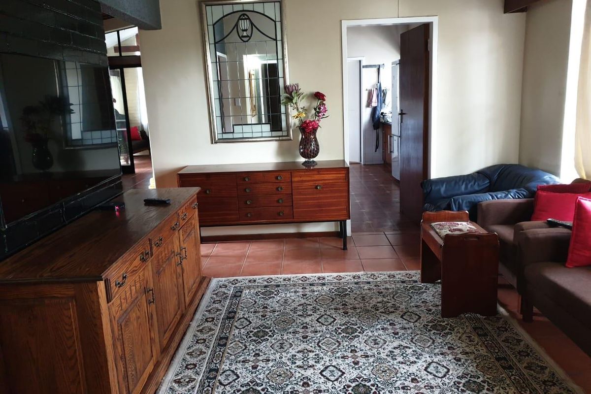 A living room featuring terracotta floor tiles and a brick fireplace surround, with an open doorway leading to an adjacent kitchen area.