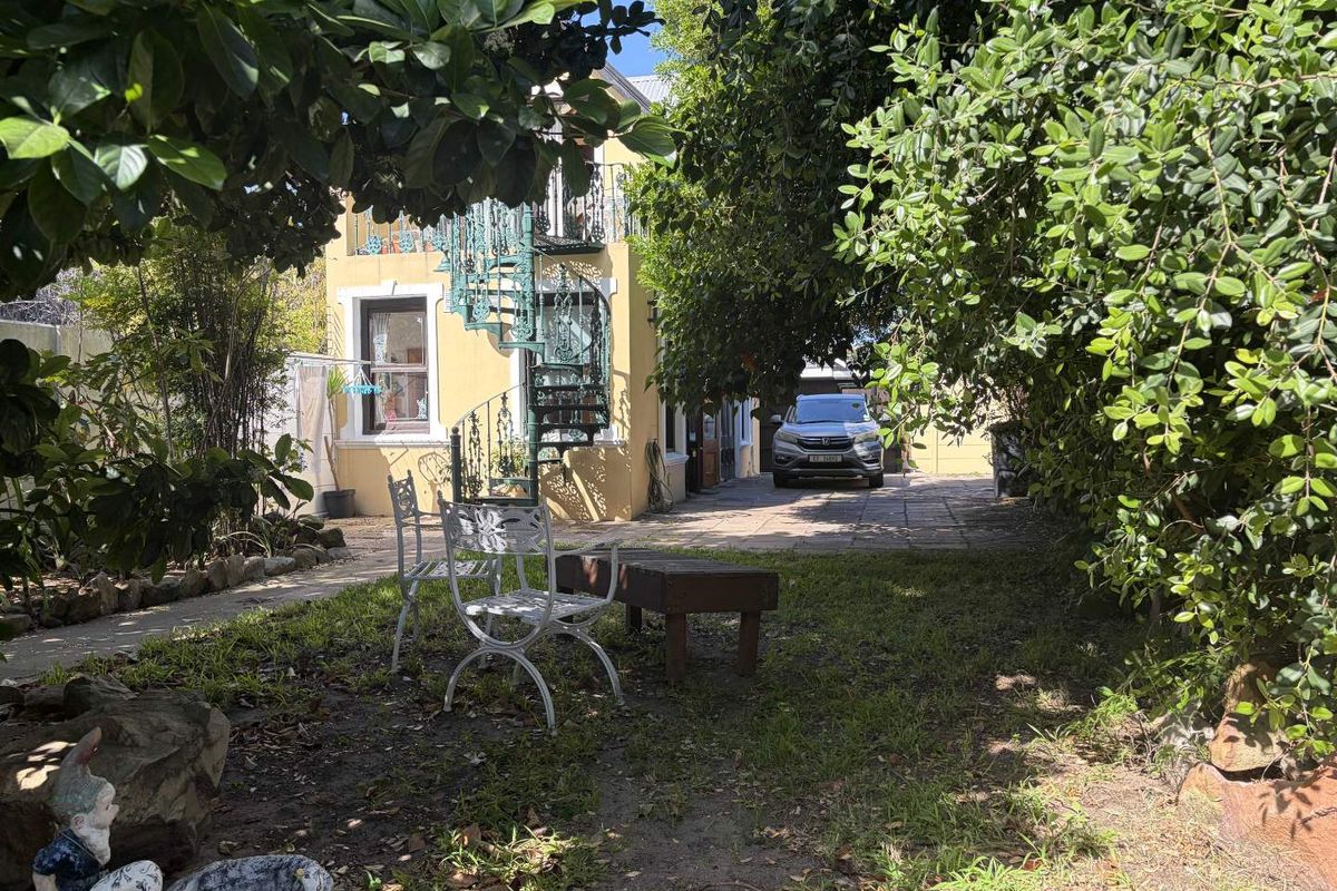 Rear view of the property featuring a paved driveway, a distinctive spiral staircase leading to an upper balcony, and established garden surroundings.