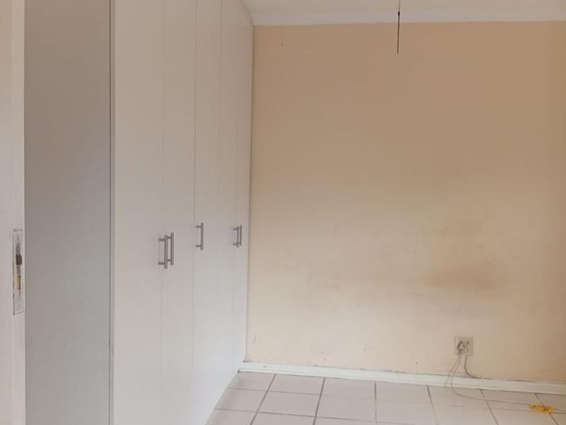 A vacant bedroom featuring built-in cupboards, a ceiling fan, and tiled flooring, requiring minor cosmetic updates to the walls and floor.
