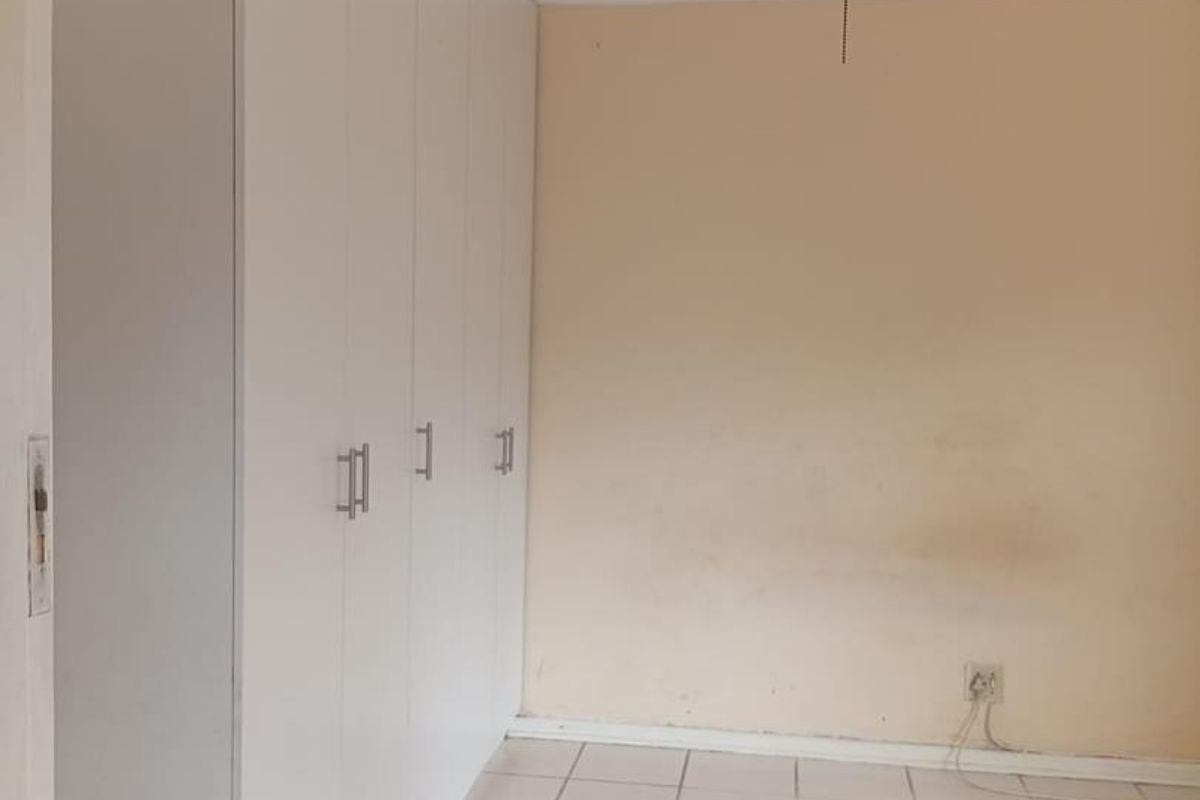 A vacant bedroom featuring built-in cupboards, a ceiling fan, and tiled flooring, requiring minor cosmetic updates to the walls and floor.