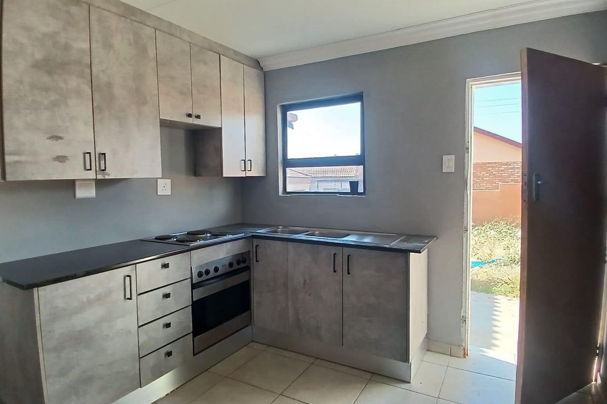 A functional kitchen featuring modern grey cabinetry, a built-in oven and hob, stainless steel sink, and direct access to the exterior.