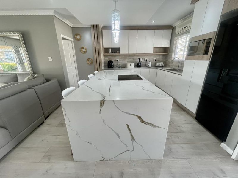 Modern open-plan kitchen featuring a large stone-topped island with integrated hob, sleek white cabinetry, and high-quality tiled flooring.