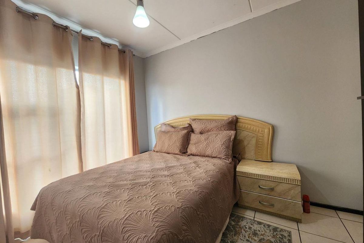 A bedroom featuring tiled flooring, neutral wall finishes, and a large window with curtain treatments.