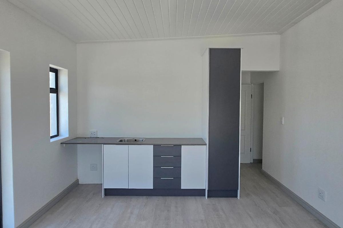A clean, modern, and empty kitchen area featuring built-in cabinetry, a sink, and light-toned laminate flooring with direct access to an outdoor patio.