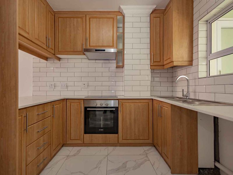 A well-maintained kitchen featuring wooden cabinetry, subway tile backsplash, built-in oven, extractor fan, and modern marble-look floor tiles.