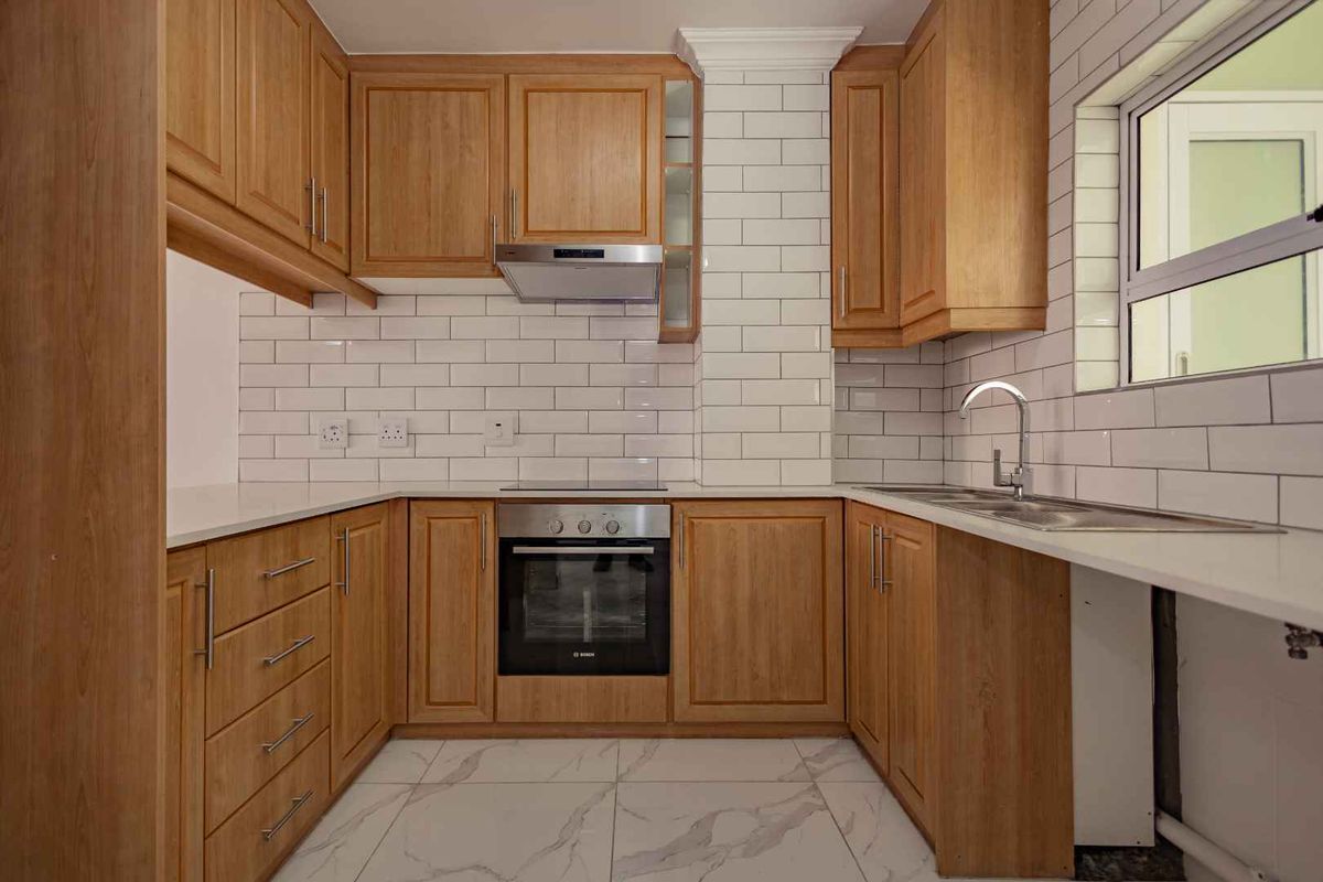 A well-maintained kitchen featuring wooden cabinetry, subway tile backsplash, built-in oven, extractor fan, and modern marble-look floor tiles.