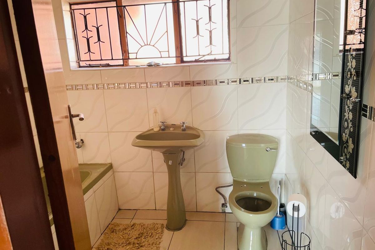 A functional bathroom featuring a pedestal basin, toilet, and bathtub with tiled finishes and security bars on the window.