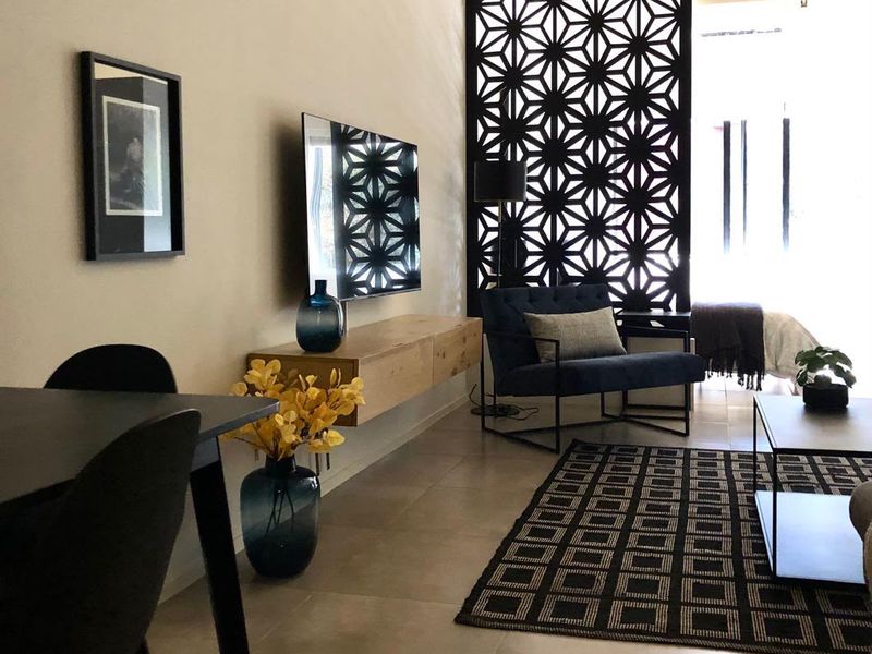 Modern open-plan living area featuring an exposed concrete ceiling, large decorative laser-cut screen divider, and neutral tiled flooring.