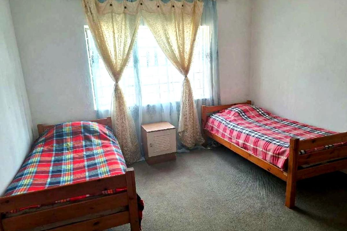 A bedroom featuring a window with security bars and carpeted flooring.