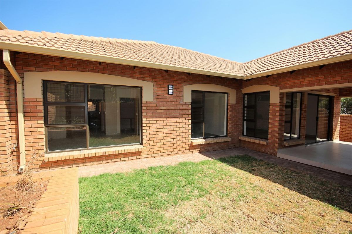 Rear view of the townhouse featuring a face brick facade, tiled roof, aluminium windows, and a small covered patio area overlooking a private garden.