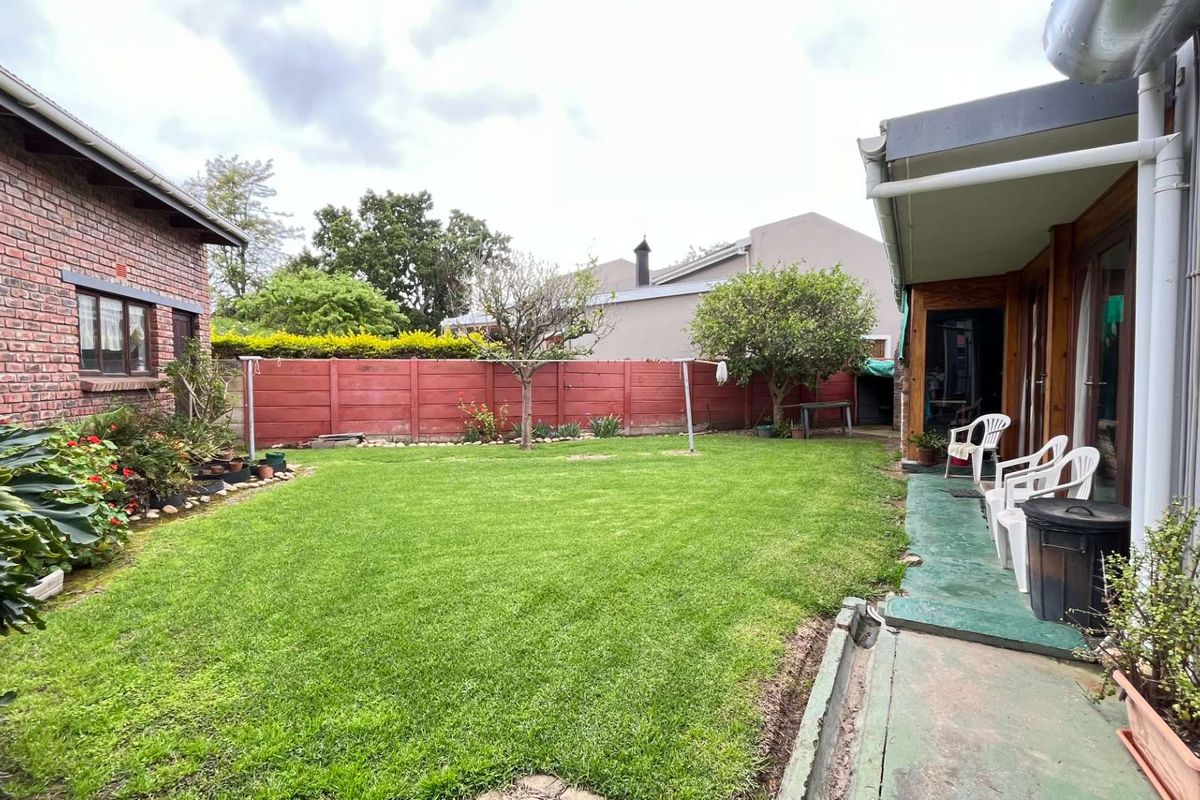 A private rear garden featuring a lawn, brick exterior wall, and a covered patio area with concrete flooring.