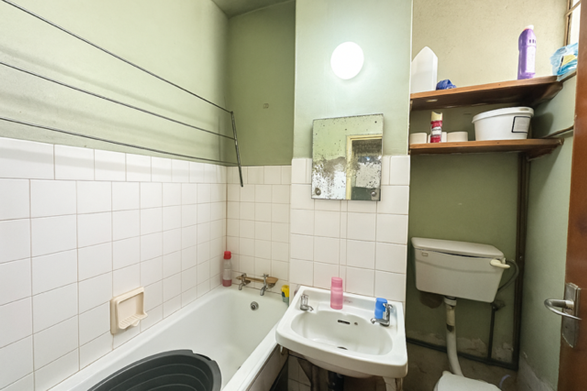 A dated bathroom featuring a standard bathtub, wall-mounted basin, and toilet, requiring cosmetic updates and modernization of fixtures and finishes.