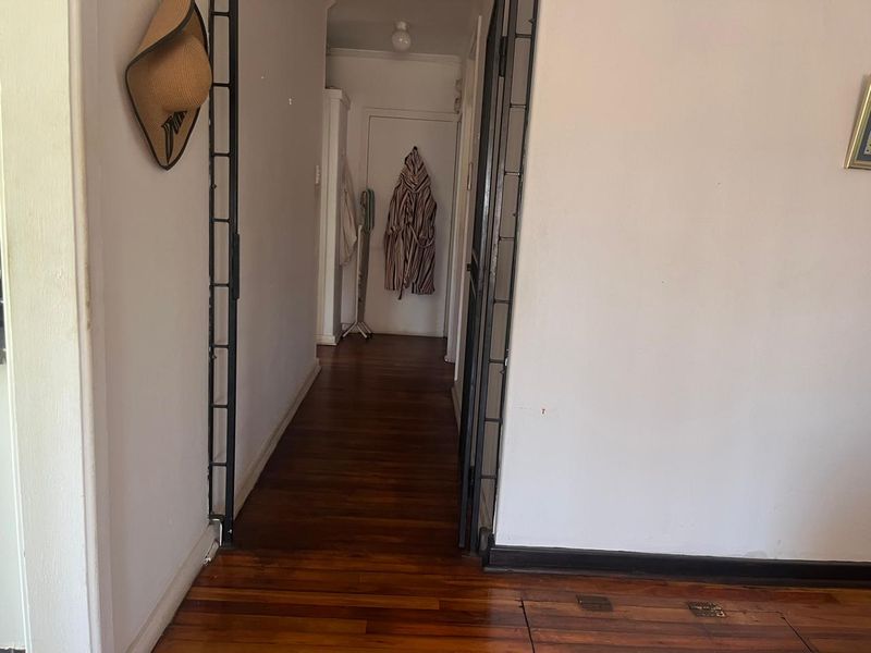 A functional hallway featuring polished hardwood flooring and a metal security gate, providing access to the interior living spaces.