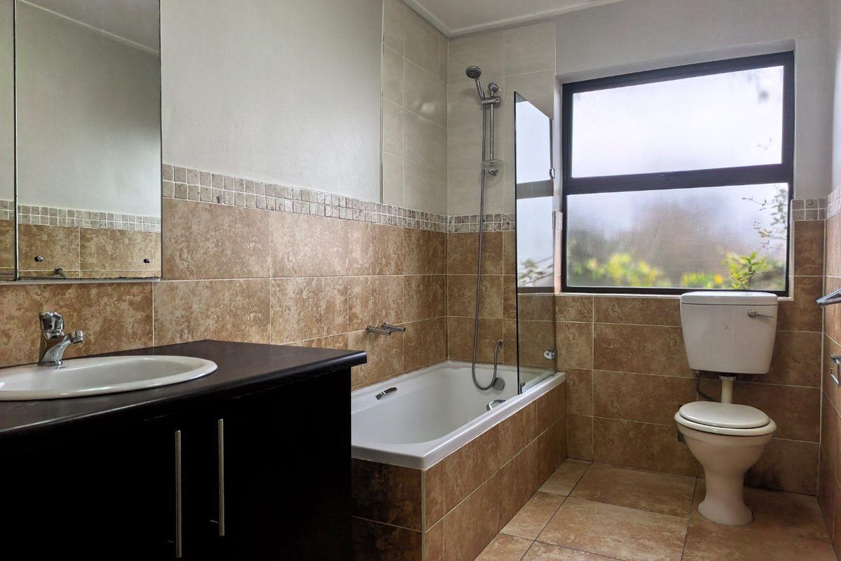A functional bathroom featuring a vanity with basin, a bathtub with shower attachment, glass screen, and a toilet, finished with neutral wall and floor tiles.