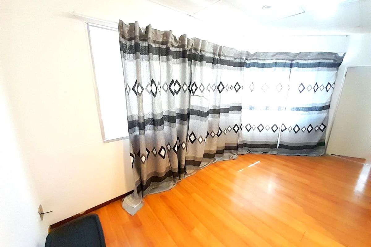 An empty living area featuring laminate flooring and ceiling tiles, awaiting personal touches to enhance the space.