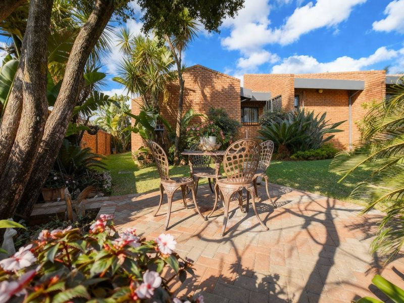 A well-maintained rear garden featuring a brick-paved patio area, established landscaping, and a classic face brick exterior facade.