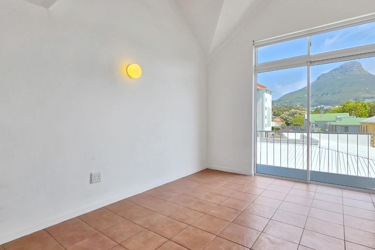 An empty bedroom featuring tiled flooring, a vaulted ceiling, and a sliding glass door leading to a balcony with mountain views.