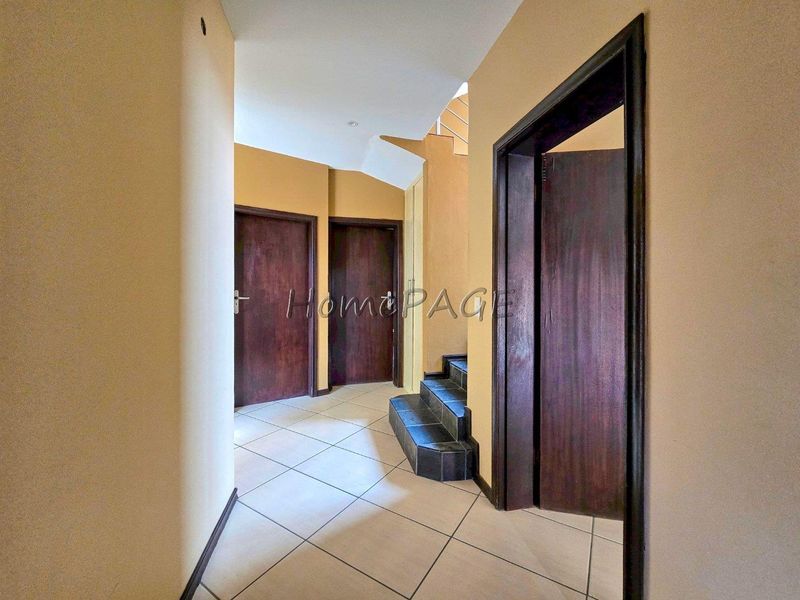 A spacious interior hallway featuring tiled flooring, dark wood-finish internal doors, and a staircase leading to the upper level.