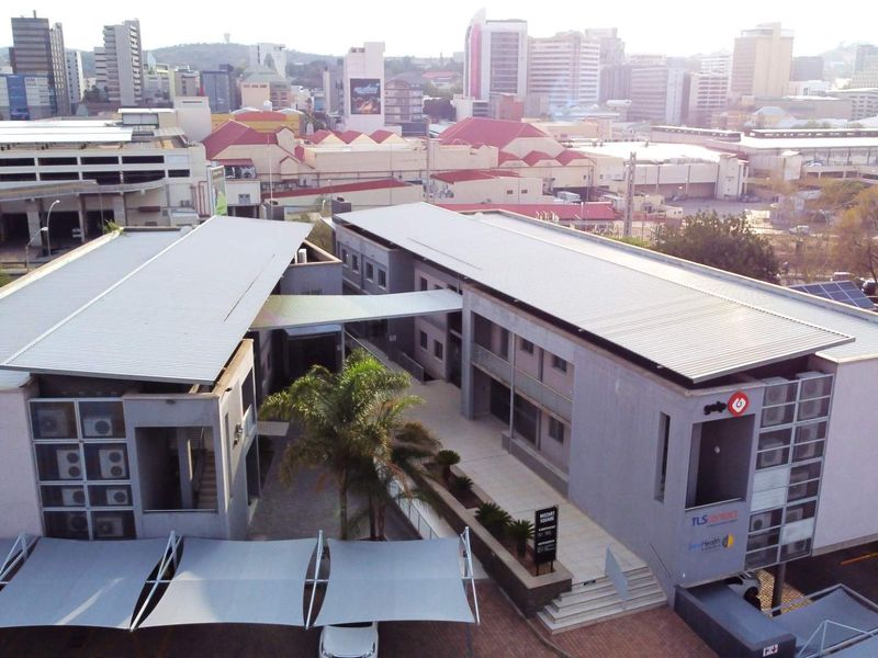Aerial view of a modern office complex featuring multiple buildings, a central courtyard, paved walkways, and integrated shade structures in an urban setting.