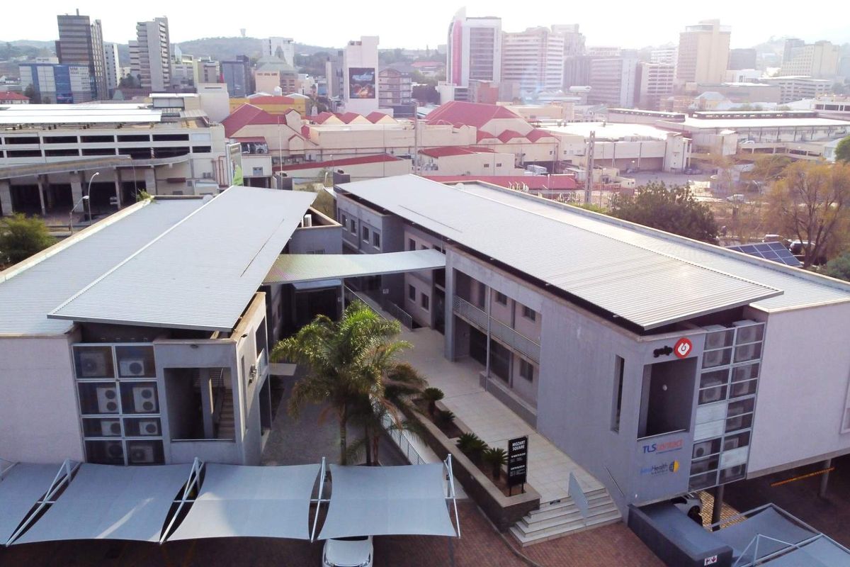 Aerial view of a modern office complex featuring multiple buildings, a central courtyard, paved walkways, and integrated shade structures in an urban setting.