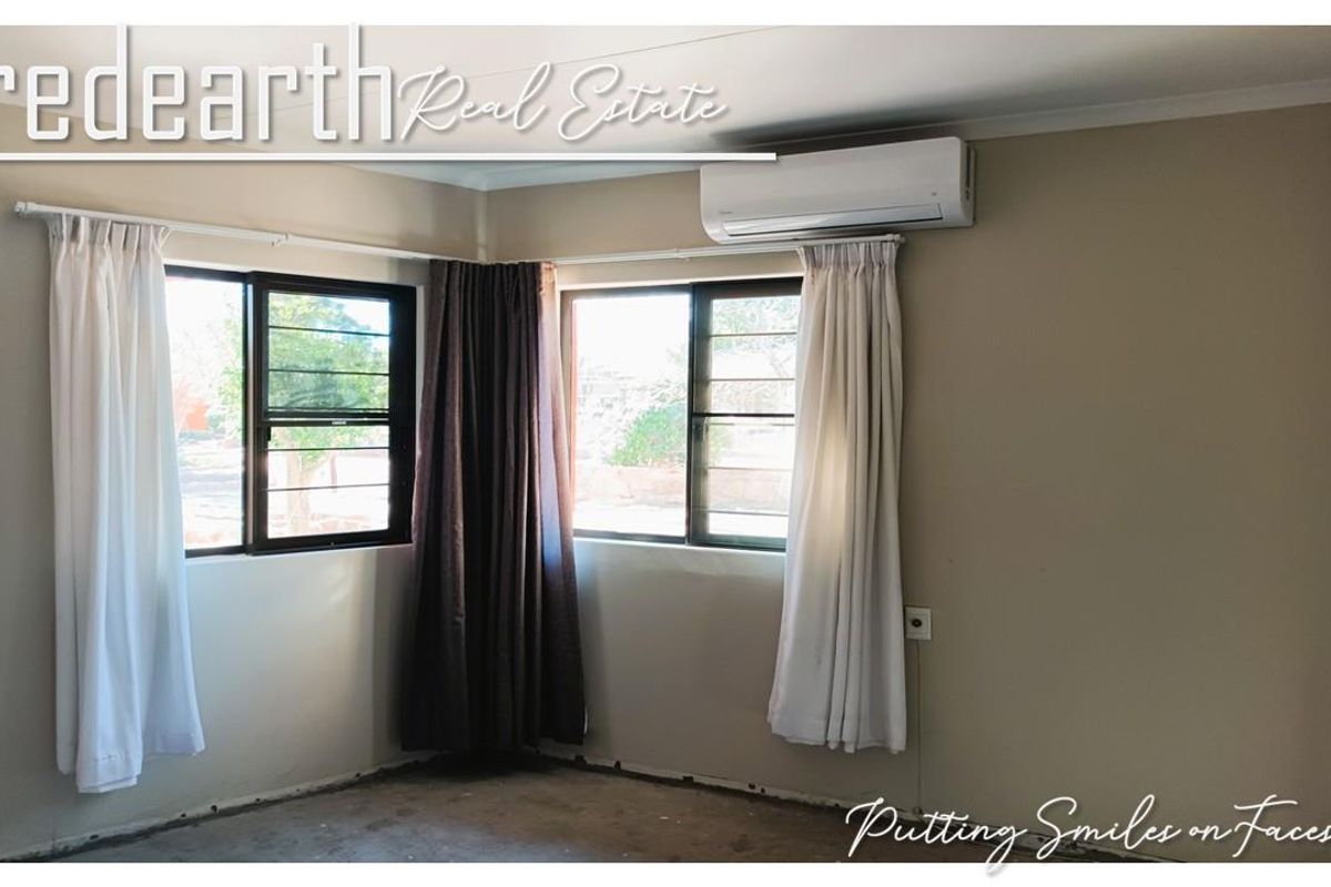 An empty bedroom featuring a wall-mounted split-system air conditioner, aluminium windows with security bars, and unfinished flooring.